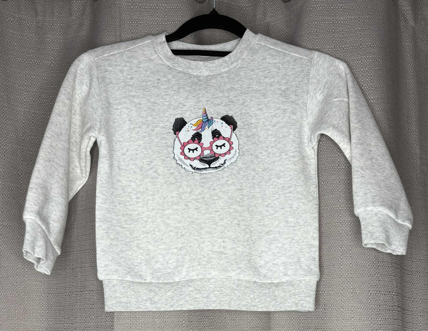 Gray sweatshirt with a panda design on a hanger against a gray background