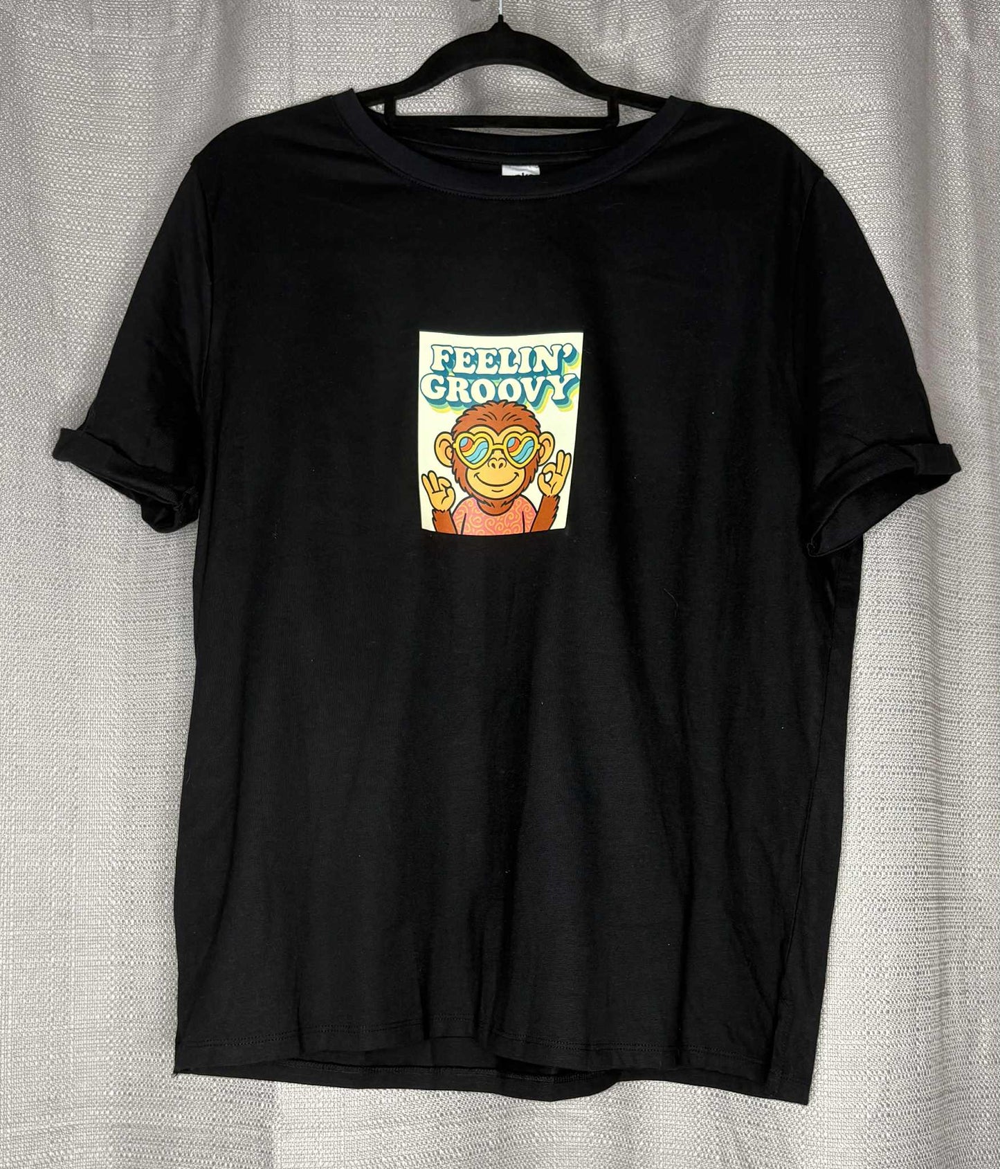 Black t-shirt with a graphic of a monkey and 'Feelin' Groovy' text on a hanger against a light gray background.
