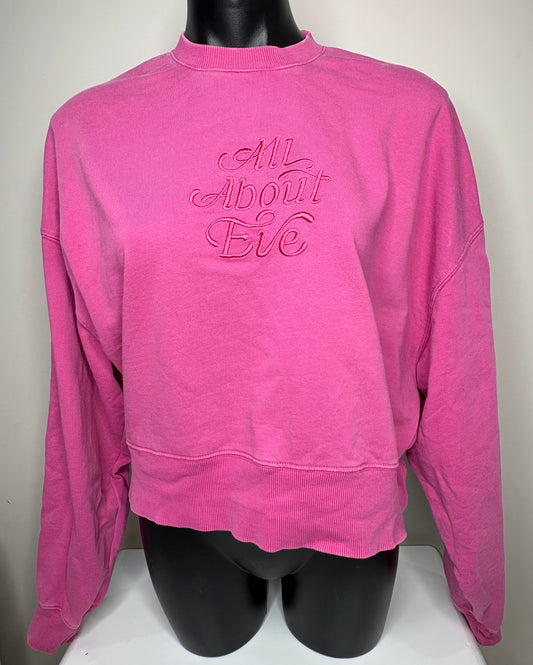 Pink sweatshirt with 'All About Eve' text on a mannequin against a white background