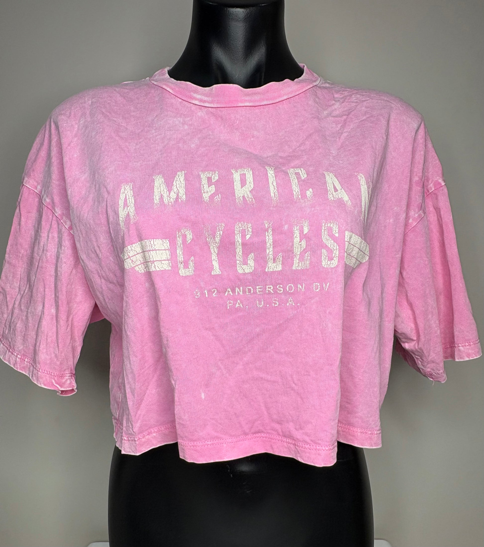 Pink t-shirt with 'American Cycles' text on a mannequin against a gray background