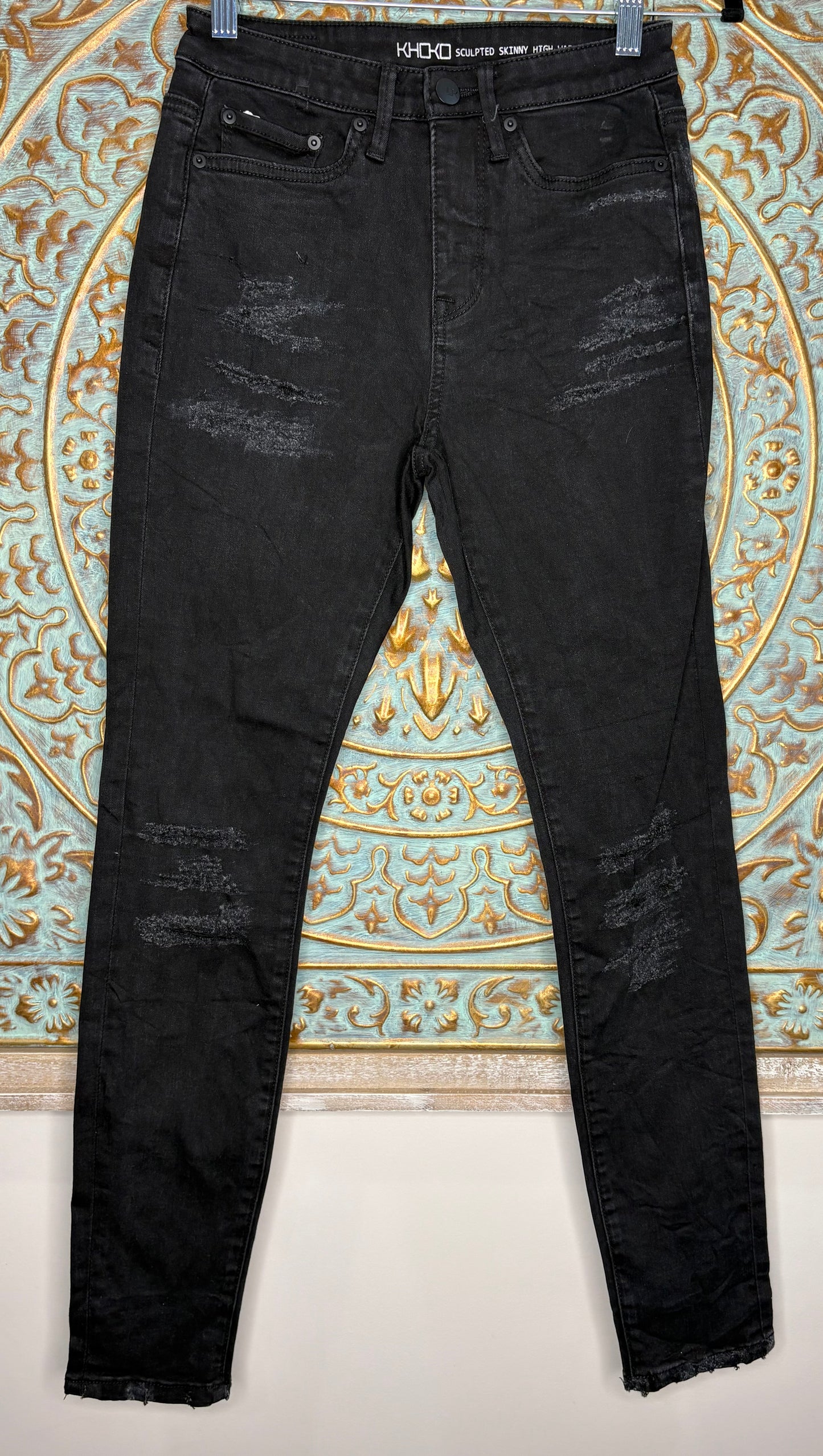 Black distressed jeans hanging against a decorative wall.