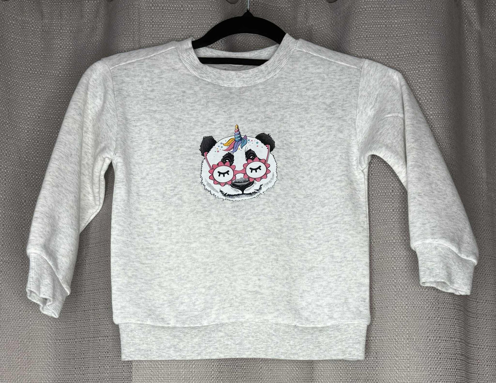 Gray sweatshirt with a panda design on a hanger against a gray background