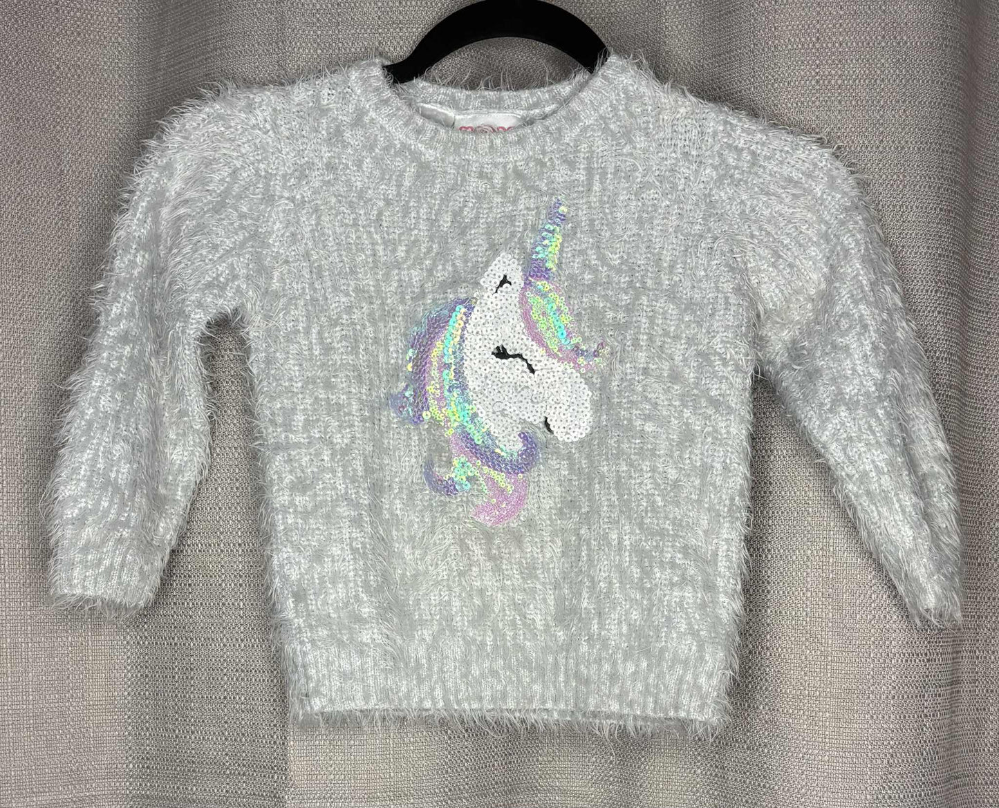 Gray sweater with a colorful unicorn design on a hanger against a gray background
