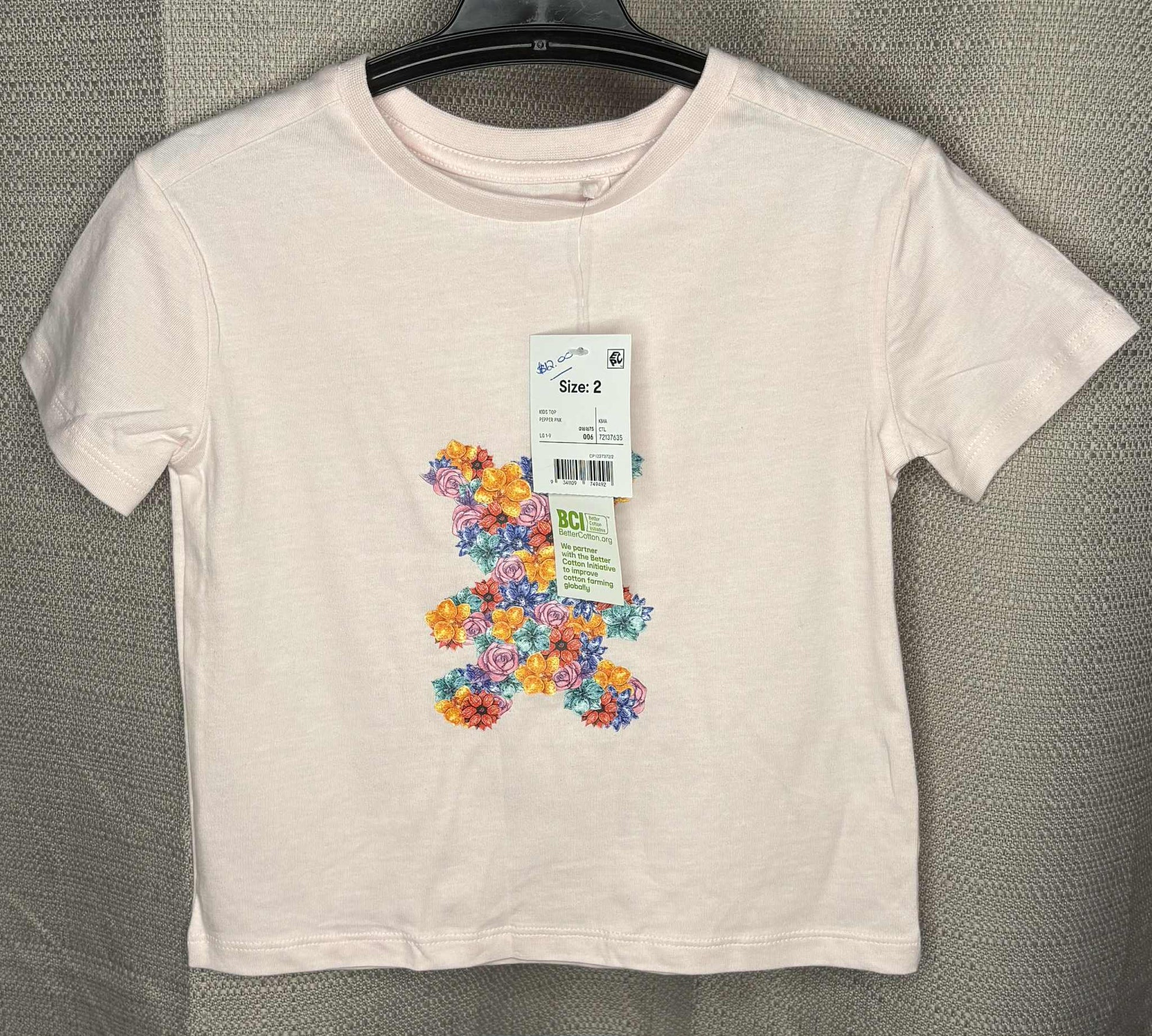 White t-shirt with colorful floral design and size tag on a gray background