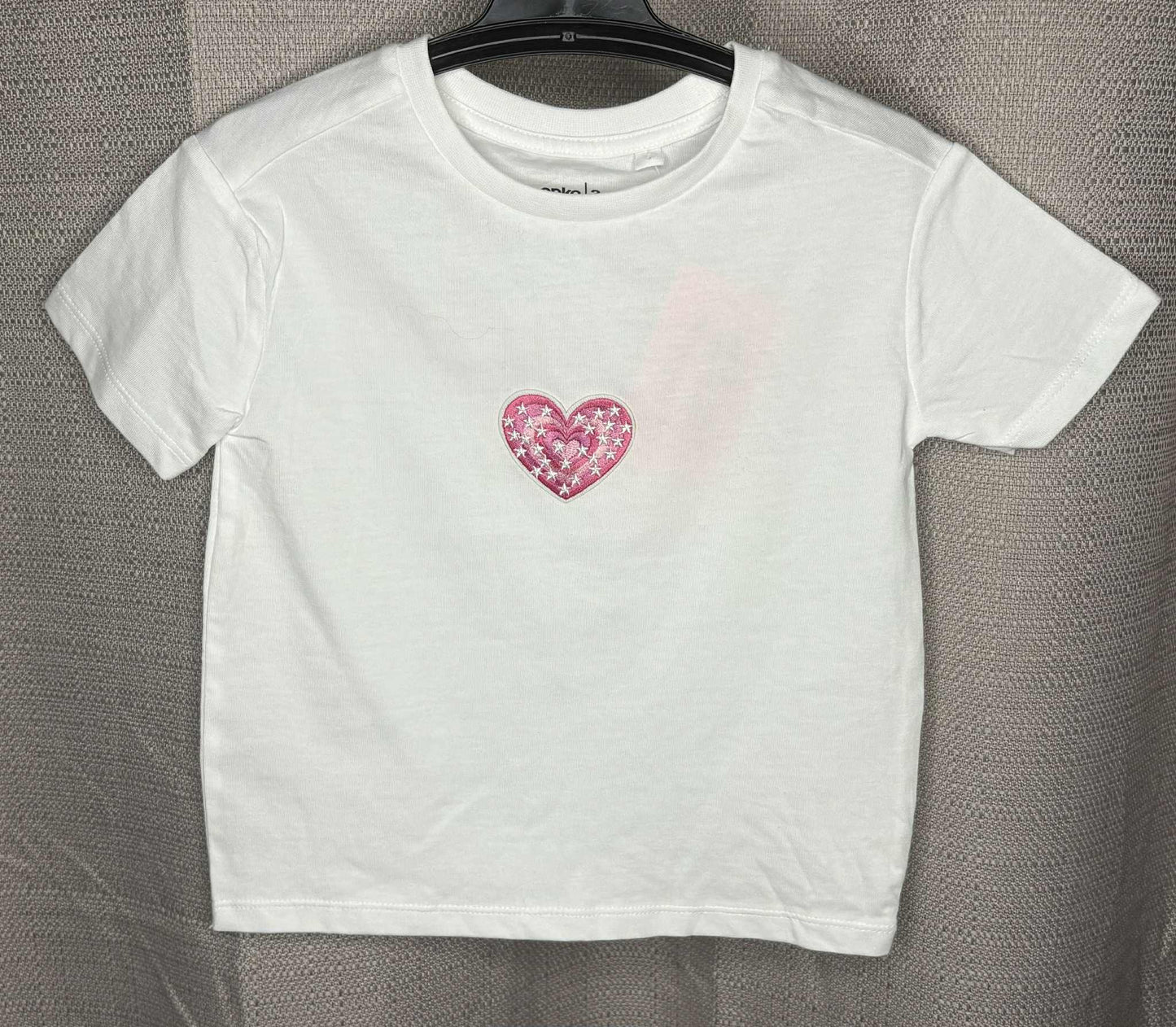 White t-shirt with a pink heart design on a gray background
