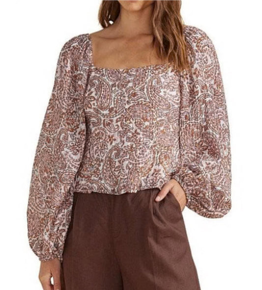 Woman wearing a patterned blouse and brown pants on a white background