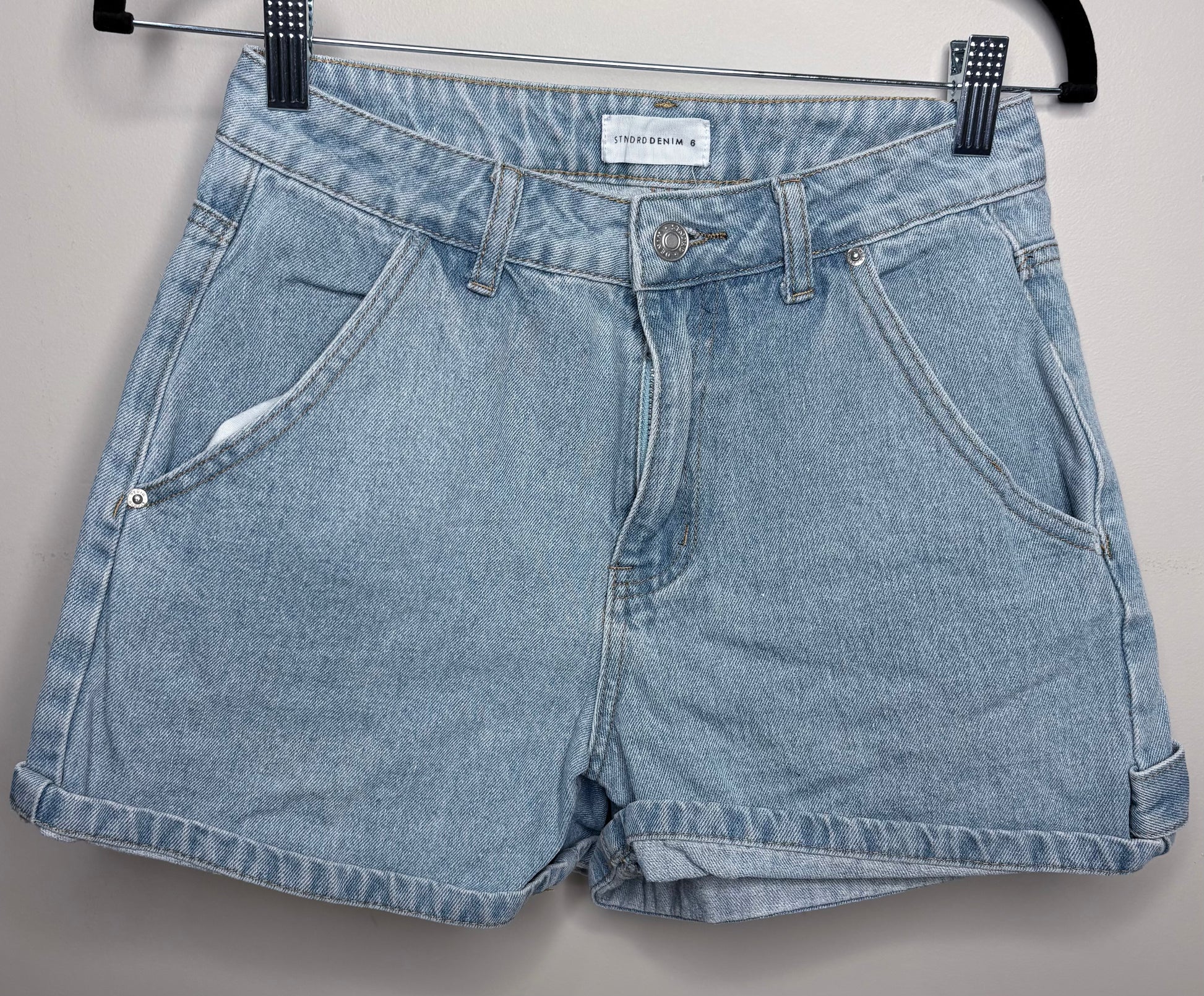 Pair of blue denim shorts on a hanger against a gray background