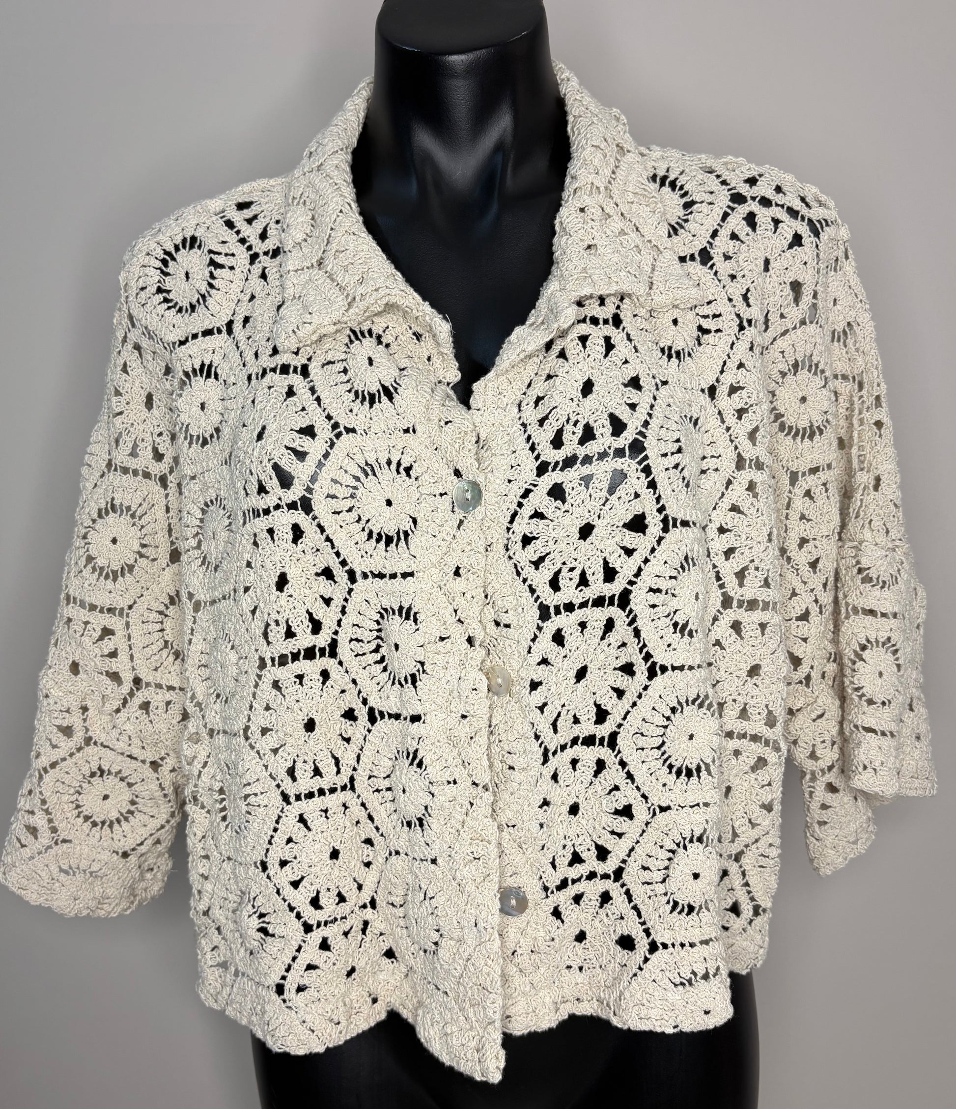 Crocheted beige cardigan on a mannequin against a gray background