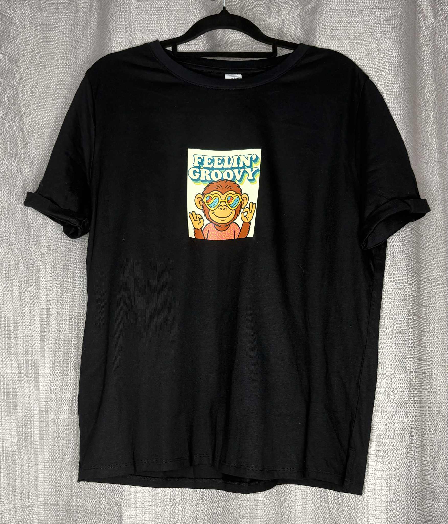 Black t-shirt with a graphic of a monkey and 'Feelin' Groovy' text on a hanger against a light gray background.